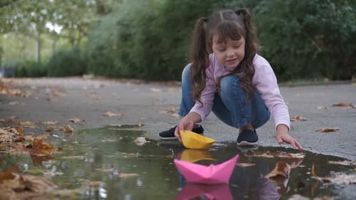 Girl Plays with Paper Boats in Puddle
