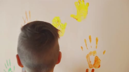Happy Mother and Her Cute Boy Having Fun Together Leaving Their Colorful Handprints on the Wall