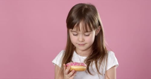 Studio Portrait of a Beautiful Little Girl Holding a Donut and Smelling Tasty Flavour
