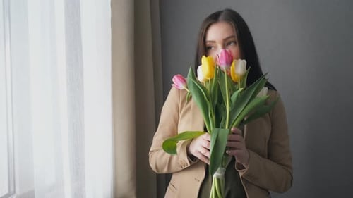 Woman Smelling Beautiful Tulips by Window