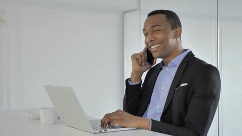 Smiling Man Talking on Phone While Using Laptop