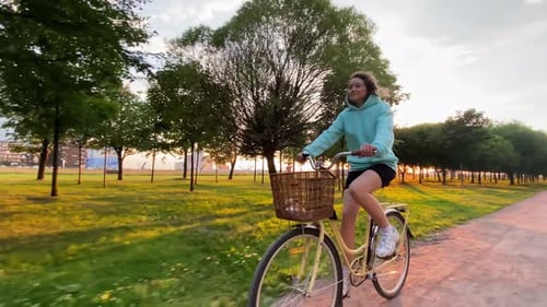 Woman in Hoodie and Shorts Rides Bicycle Along Rural Road