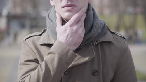 Close-up of Young Sick Man Couching and Rubbing Throat. Portrait of Ill Caucasian Guy Outdoors on