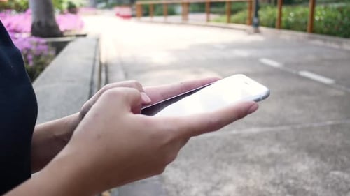 sian young woman sitting at bench in park using smartphone for talking, reading and texting.
