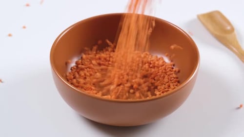Orange Lentils Falling into Brown Ceramic Bowl