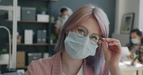 Slow Motion Portrait of Cheerful Young Woman Touching Glasses Wearing Mask in Office