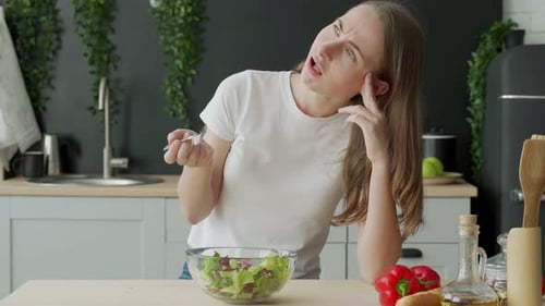 Unglückliche Frau isst Gemüsesalat am Tisch in Küche