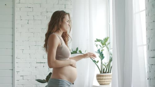 Une femme
enceinte ressent une douleur enceinte à la maison. Fenêtre debout pour femmes enceintes en gros plan