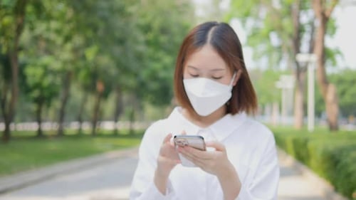 Woman Walks in Park Using Phone With Mask