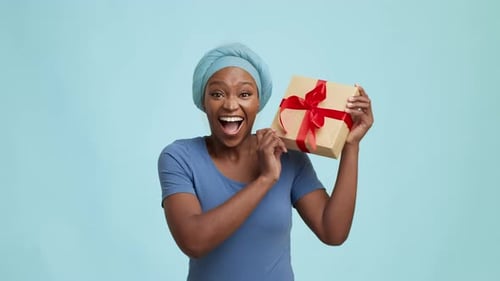 Joyful Black Lady Shaking Gift Box Standing Over Blue Background