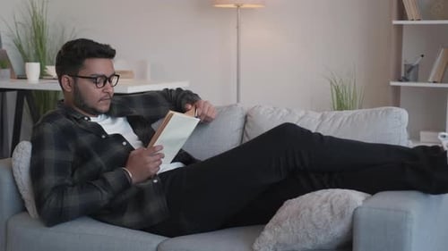 Young Adult Reading a Book Lying on Sofa