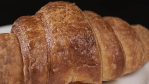 Croissant auf weißem Teller rotierend vor der Kamera auf schwarzem Hintergrund