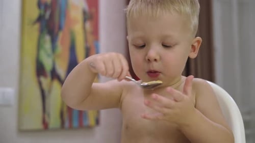 Blonde Child Eating Food with Spoon Indoors