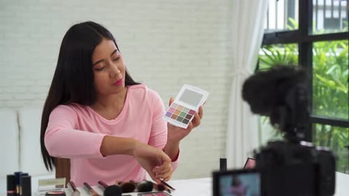 La bloguera de belleza presenta cosméticos de belleza mientras está sentada frente a la cámara para grabar un vídeo con un cepillo.