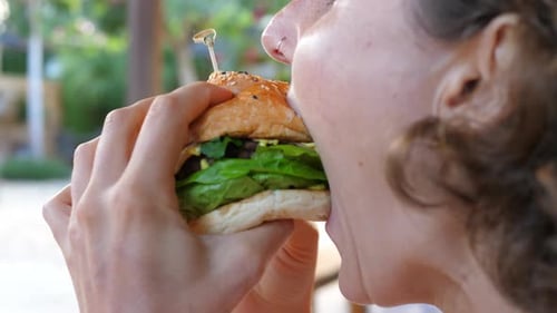 Close Up of Curly Woman Holding in the Hands and Biting Vegan Falafel Burger for Dinner