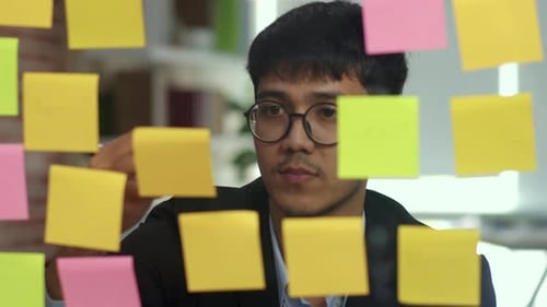 Asian creative man stick a sticky note on glass board.