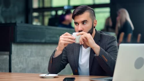 Konzentrierter gutaussehender Geschäftsmann genießt Kaffeepause im Café während der Arbeit mit Laptop-PC