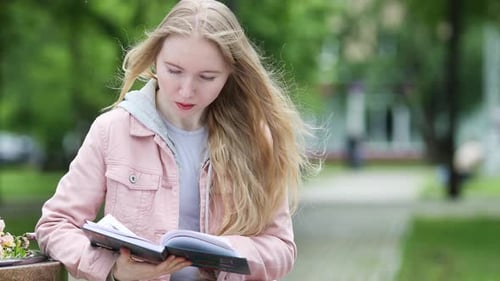 Young Woman Reading Book Outdoors in City Park