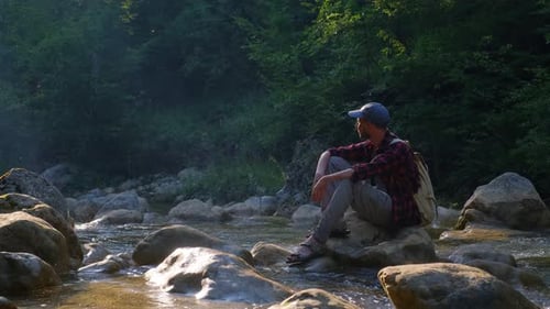 Männlicher Reisender genießt die Schönheit der Natur am Fluss im Wald bei Sonnenuntergang
