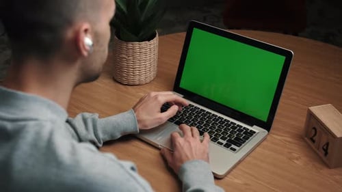 Young Caucasian Man Using a Laptop Green Screen on the Desk at Home.