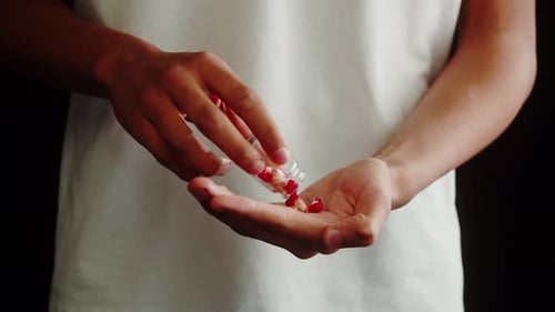 Person pours pills into hand from bottle