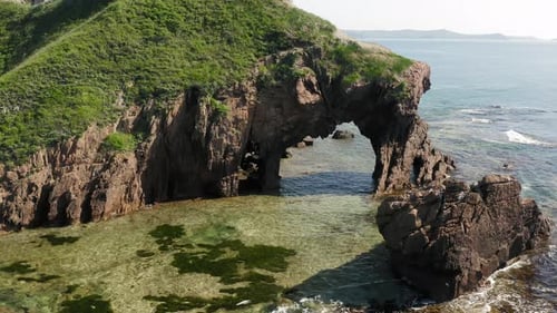 Drohnenaufnahme eines Natursteinbogens an der Küste an einem sonnigen Tag