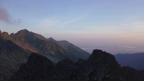 Wide aerial view high above rocky peaks of mountains and sunset sky background. Colorful evening sky