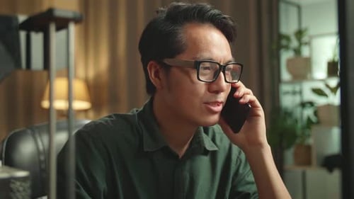 Asian Man Talking On Mobile Phone While Works On Personal Computer And 3D Printer In Home Office