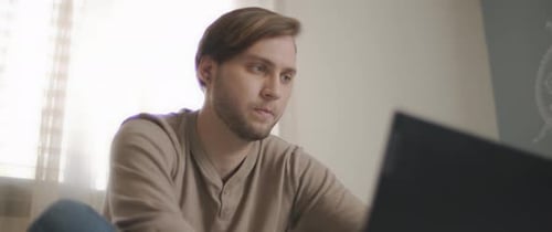 A close up of a young man sitting in bed and working on a computer.