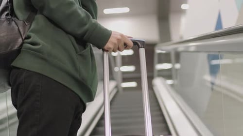 Young Adult with Suitcase on Escalator with Headphones