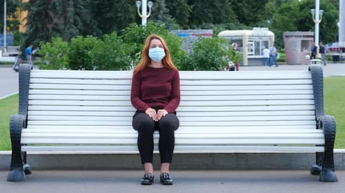 Pandemic, Coronavirus Quarantine. Young Woman Sits on a Park Bench Alone