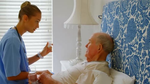 Side view of young Caucasian female doctor discussing medication with senior man on bed at home 4k