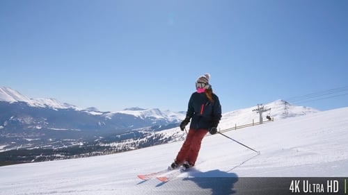 4K Slow Motion Pan of Skier Turning with Mountains and Ski Lift in the Distance