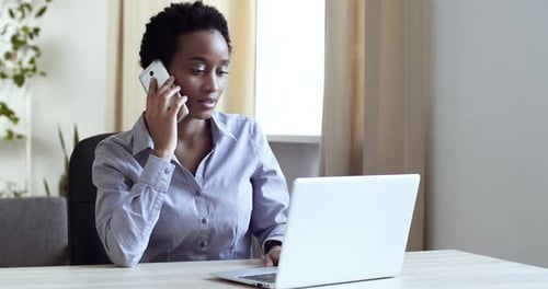 Professional Woman Working at Desk on Laptop, Talking on Phone