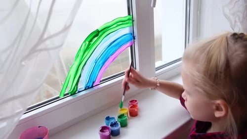 Child Paints Colorful Rainbow on Window at Home