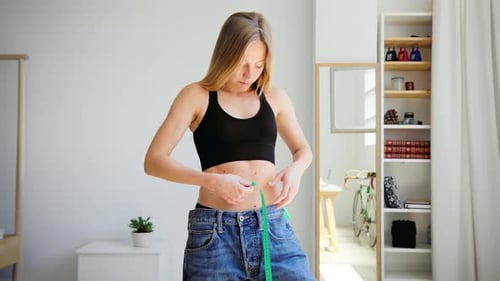 Woman Measures Waist with Measuring Tape in Home