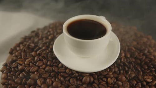 Steaming Coffee Cup on Roasted Coffee Beans