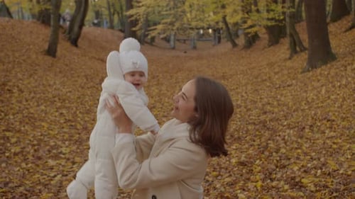 Woman Lifts Baby Up in Colorful Autumn Park
