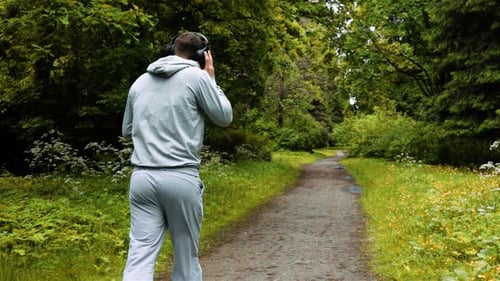 Male Runner in Warm Clothes in Autumn Park Listening To Music and Hood Clothes.