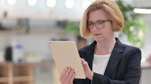 Senior Woman Celebrates Success Using Tablet in Office