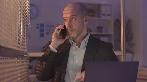 Businessman Talking on Cellphone in Office at Night