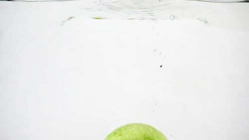 The Green Apple Falls Into the Water. Isolated Apple on White Background in Slow Motion