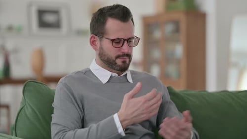 Man Rubbing Eyes Sitting On Couch Indoors