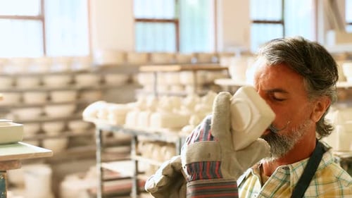 Man Inspecting Pottery in a Sunlit Workshop