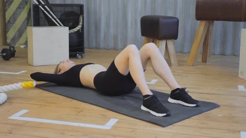 Entraînement des muscles abdominaux. Dame concentrée faisant des exercices de crunches, allongée sur le sol au gymnase, Ralentissement