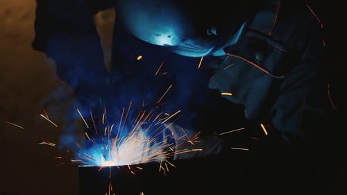 Ein Schweißer in einem Schutzhelm und Kleiderschweißnähte, Metallfunken beleuchten ihn