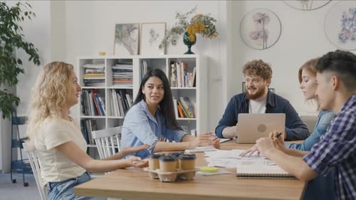 Group of Young Men and Women are Sitting at Table in Modern Office and Discussing Business Issues in