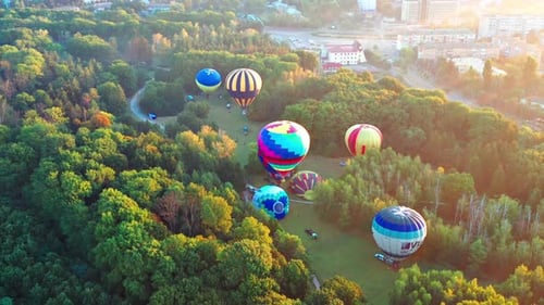 Beautiful sunbeams illuminate the balloons that fly over the park, green trees.