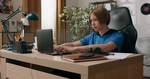 A Young Boy Uses Laptop While Sitting in Room on a Chair at Desk