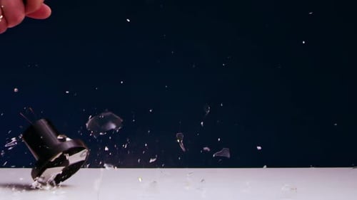 AMan's Hand Smashes Incandescent Light Bulb Lying on Table with Iron Hammer
